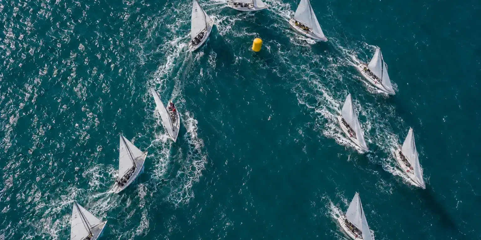 Sailboats rounding a yellow buoy, seen from above